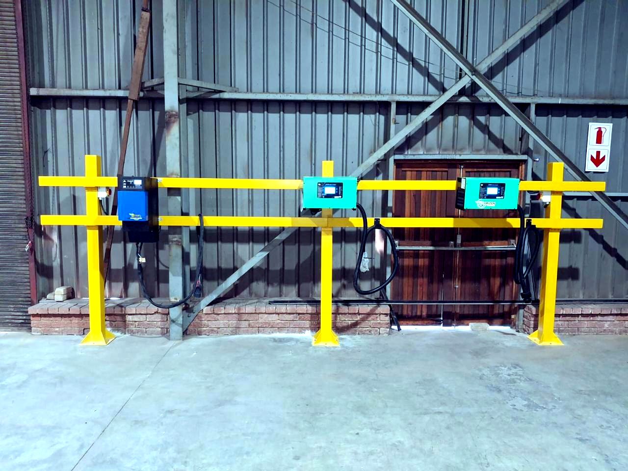 Wall-mounted battery chargers installed at a guard-railed battery bay in a warehouse.