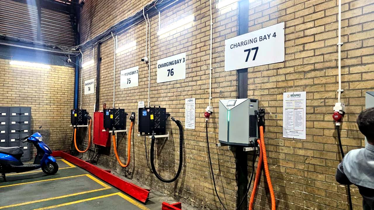 Row of wall-mounted battery chargers at numbered charging bays in a warehouse, with cables connected and ready for use.